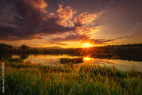 Krajobraz wodny. Widok na jezioro i zachód słońca. Piękny zachód słońca nad jeziorem ze starą łodzią i bezchmurnym niebem w tle, Polska