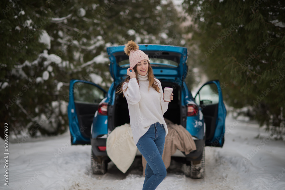 a young happy girl in a white sweater walks through the woods in winter and warms up with coffee or tea