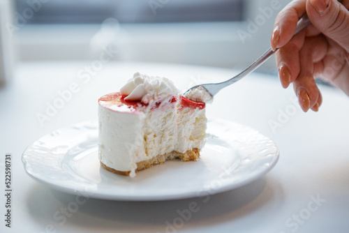 Red and white cake being cut with fork in female hand.