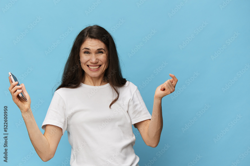 portrait of a beautiful, pleasant woman with long hair, in a light T-shirt, holding a fashionable smartphone in her hands and joyfully raising her hands up. Horizontal photo on a light blue background portrait of a beautiful, pleasant woman with long hair, in a light T-shirt, holding a fashionable smartphone in her hands and joyfully raising her hands up. Horizontal photo on a light blue background