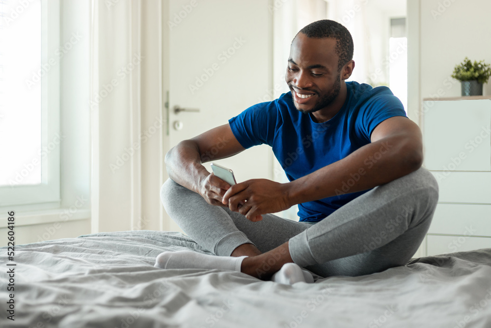 Black Man Using Smartphone Texting Sitting In Bedroom At Home Black Man Using Smartphone Texting Sitting In Bedroom At Home