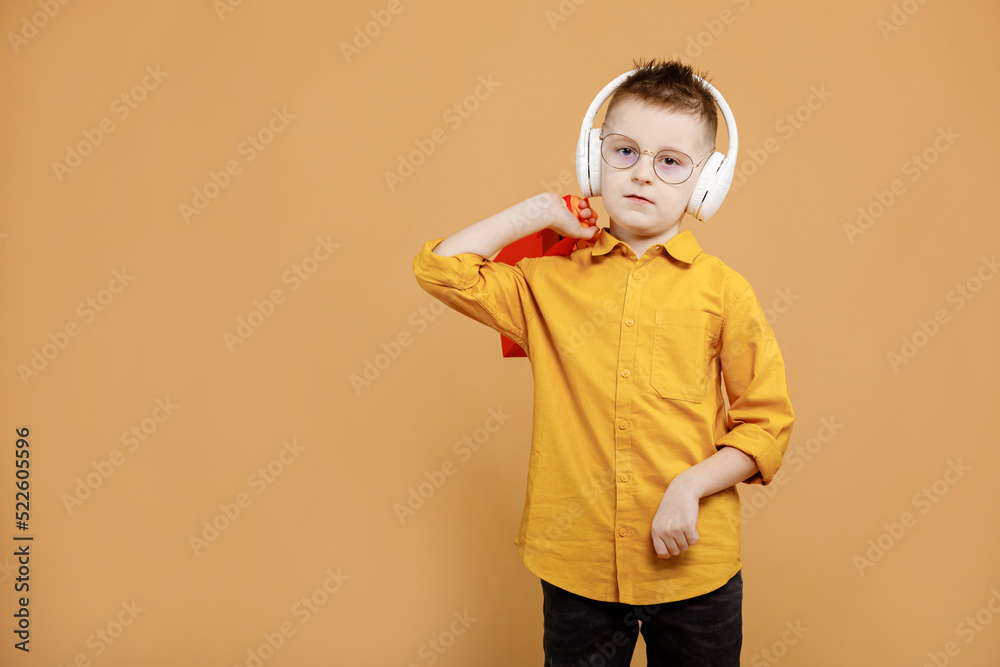 Image of smiling boy holding bags with presents or shoppings on yellow background. child in white headphone. Shopper with many colored paper bags. Holidays sales and discounts. Cyber monday Image of smiling boy holding bags with presents or shoppings on yellow background. child in white headphone. Shopper with many colored paper bags. Holidays sales and discounts. Cyber monday
