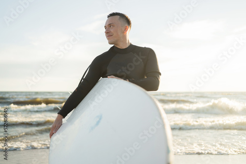 A male surfer on a surfboard wetsuit goes to play sports in the sea