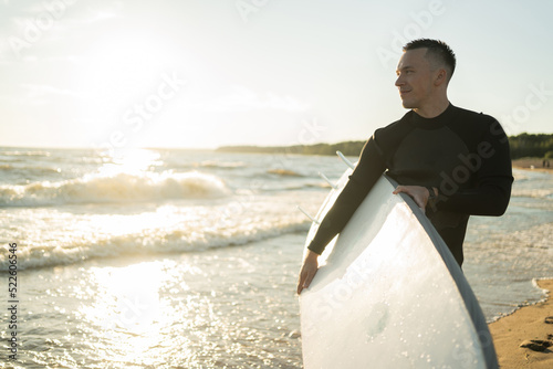 A male surfer on a surfboard wetsuit goes to play sports in the sea