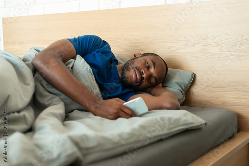 African American Guy Using Phone Texting Lying In Bedroom Indoor
