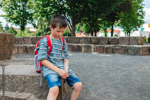 Foto A sad schoolboy sits in the school yard with a backpack on his back