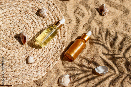 Hyaluronic acid and shine oil or serum on sandy beach with palm leaf shadow, straw and shells, summer skin care concept, top view, flat lay image.