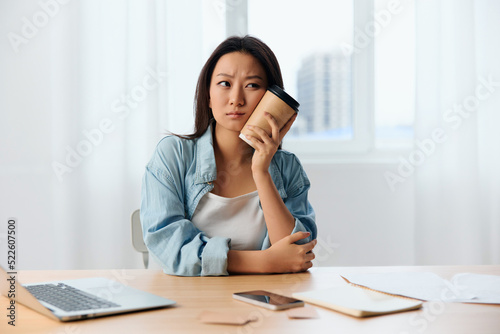 Upset frustrated pensive young Asian cute female businesswoman reclines on coffee cup looks aside in light office interior. Freelancer work at home. Lady corporation leader concept. Copy space Offer