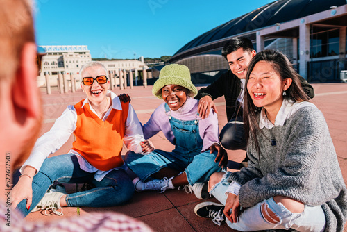Group of diverse friends laughing and talking sitting on the floor outdoors. © Jose Calsina