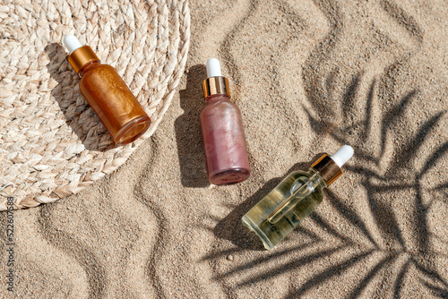 Hyaluronic acid and shine oil or serum on sandy beach with palm leaf shadow, summer skin care concept, top view, flat lay image.