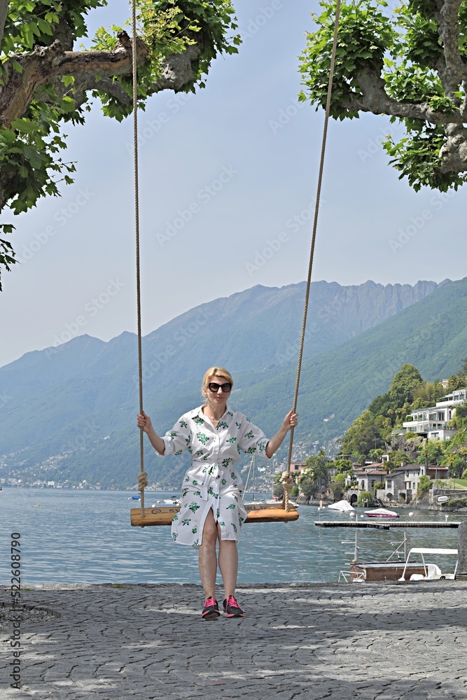 young woman in sunglasses swings on a swing near the lake