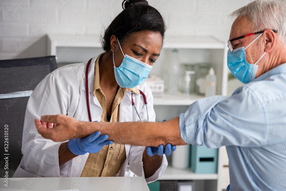 Female doctor is examining male elderly patient at clinic. Doctor and patient wearing a face mask. Female doctor is examining male elderly patient at clinic. Doctor and patient wearing a face mask.