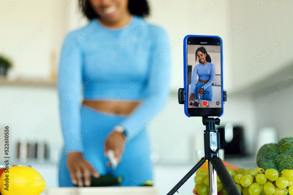 Ταπετσαρία Slim african american woman in sportswear preparing fresh salad and shooting vid