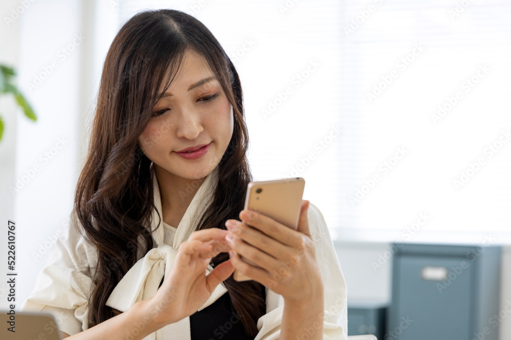 A Japanese woman checking smartphone by remote work in the small office A Japanese woman checking smartphone by remote work in the small office