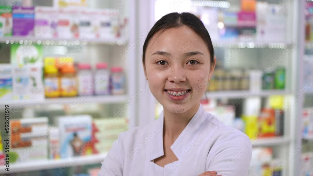 Back view young slim Asian woman examining pills on shelves in pharmacy turning looking at camera smiling. Close-up cheerful beautiful pharmacist posing in drugstore. Intelligence and lifestyle Back view young slim Asian woman examining pills on shelves in pharmacy turning looking at camera smiling. Close-up cheerful beautiful pharmacist posing in drugstore. Intelligence and lifestyle