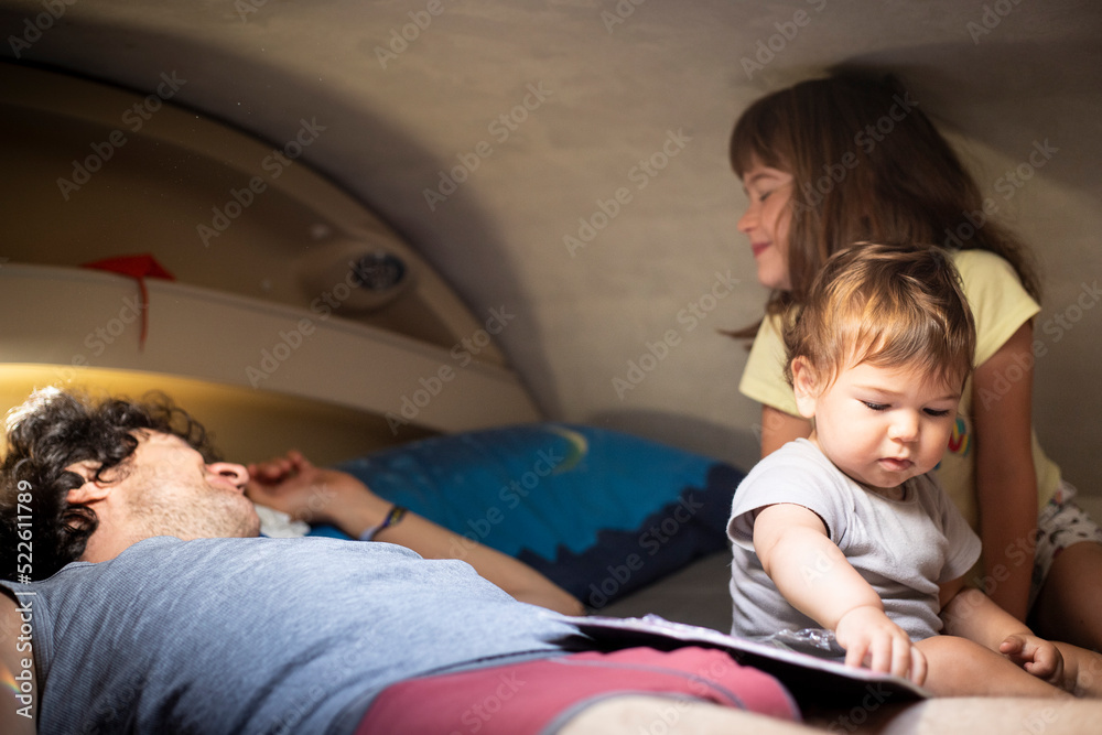 Young caucasian father and two children having fun at bedtime on an overcab bed in a motorhome or campervan. Camper vacations with children.