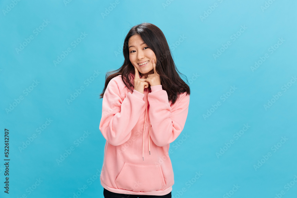 Happy lovely Asian student young lady in pink hoodie sweatshirt smiling posing isolated on over blue studio background. The best offer for ad. People Emotions for Everyday concept Happy lovely Asian student young lady in pink hoodie sweatshirt smiling posing isolated on over blue studio background. The best offer for ad. People Emotions for Everyday concept