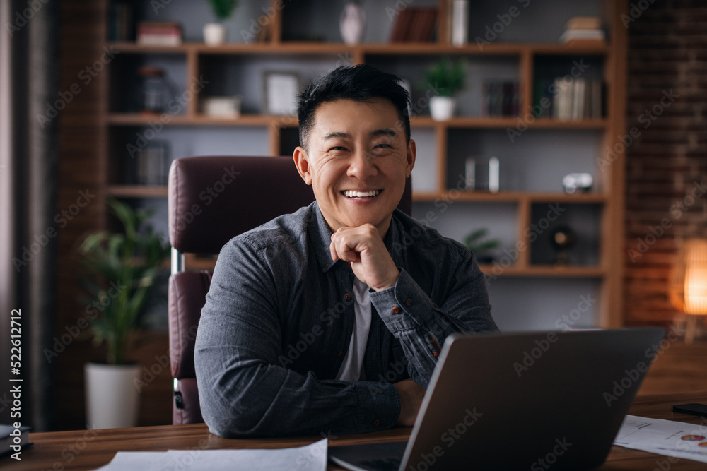 © Prostock-studio - Smiling successful handsome adult korean man at workplace with laptop look at camera © Prostock-studio - Smiling successful handsome adult korean man at workplace with laptop look at camera