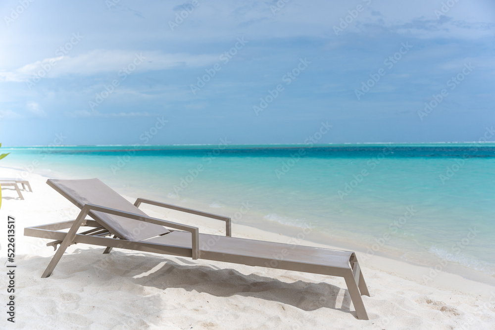 Beautiful tropical beach with white sand and sun lounger on background of turquoise ocean and blue sky with clouds. Luxury resort in Maldives 2022