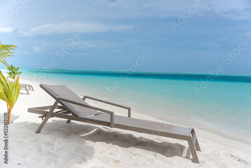 Beautiful tropical beach with white sand and sun lounger on background of turquoise ocean and blue sky with clouds. Luxury resort in Maldives 2022