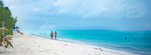 Couple walking along the beach with turquoise water  in tropical paradise  in Maldives Island 2022 