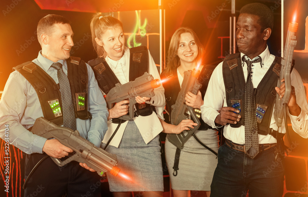 Group of glad co-workers holding laser guns and posing at laser tag room