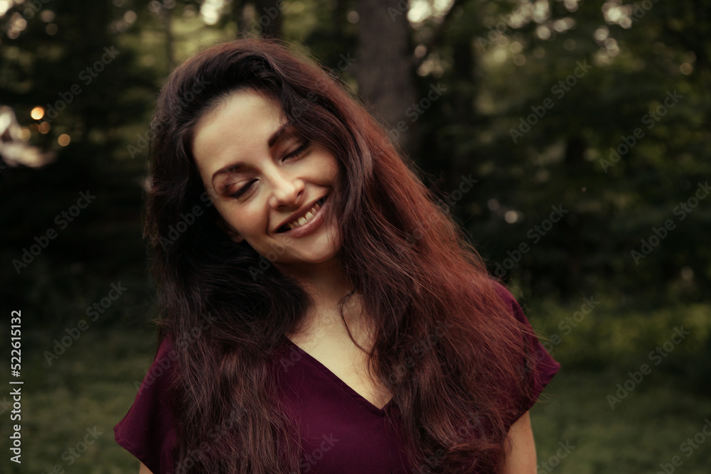Beautiful enjoying relaxing woman with happy toothy smile and brown long hair and closed eyes on nature trees summer green background in the park. Closeup happy lifestyle portrait. Vintage Beautiful enjoying relaxing woman with happy toothy smile and brown long hair and closed eyes on nature trees summer green background in the park. Closeup happy lifestyle portrait. Vintage
