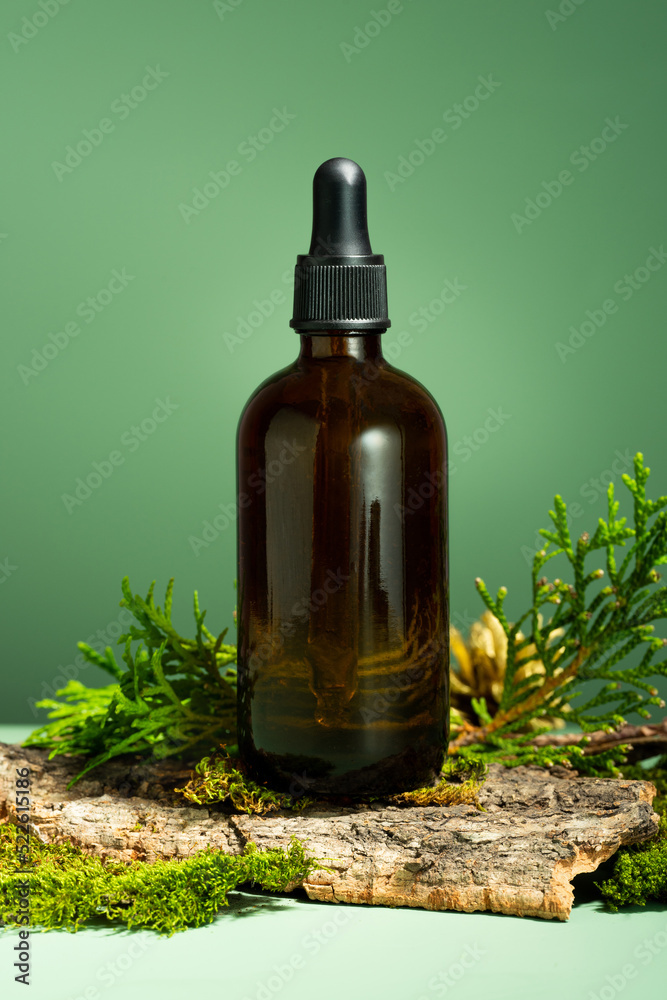 Glass bottle of body oil. A conceptual composition of essential oil, moss and tree bark on a green background. Oil serum for skin and hair care. Self-care and wellness, Forest and nature theme