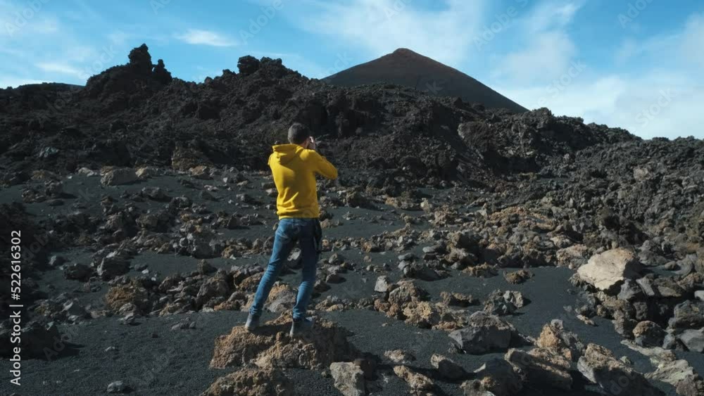 Man traveler walks through the lava field around Chinyero volcano in the Teide national park on the island of Tenerife. Go Everywhere. Surface of another planet. Slow motion shot Man traveler walks through the lava field around Chinyero volcano in the Teide national park on the island of Tenerife. Go Everywhere. Surface of another planet. Slow motion shot
