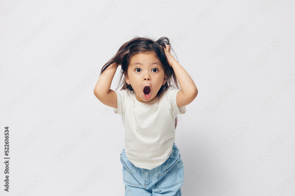 funny, cute, little girl stands in a white T-shirt on a light background and raises her hair on her head up