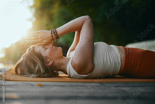 Tableau sur toile A mindful woman is lying on her back and holding hands in a namaste position while practicing breathing on the dock near the river in nature