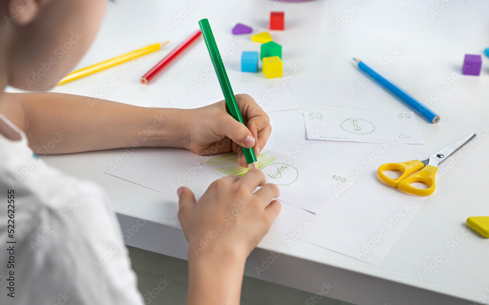 A little boy enthusiastically draws toy money with colored pencils for the game. Family budget. Economy. Money. The kid draws. Economic crisis. Kids play. Selective focus. A little boy enthusiastically draws toy money with colored pencils for the game. Family budget. Economy. Money. The kid draws. Economic crisis. Kids play. Selective focus.
