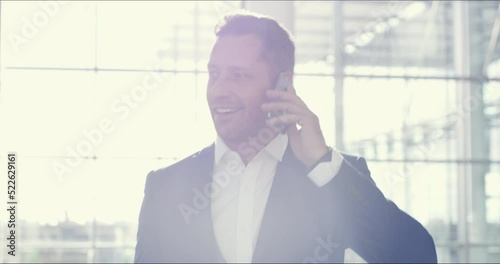 Successful businessman on a phone call with a happy client while walking to work inside a modern building. Smart, confident and proud male entrepreneur calling and talking to an executive manager photo