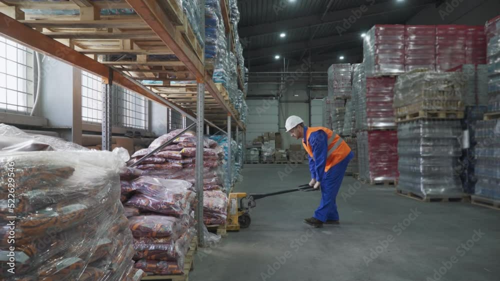 Factory worker uses the pallet handling equipment at the warehouse. Worker moving the supply with a manual pallet jack equipment. Worker transporting the items with pallet carrier equipment