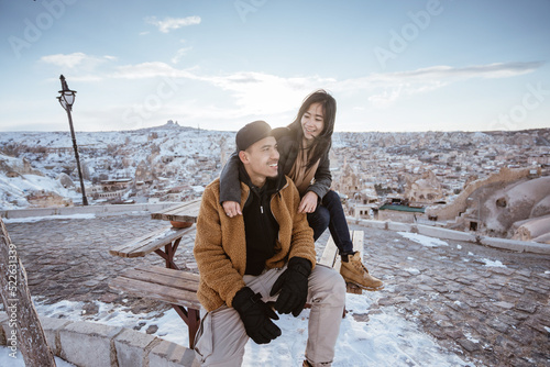 asian couple sitting on a bench enjoying the view from top with a beautiful snowy valley landscape
