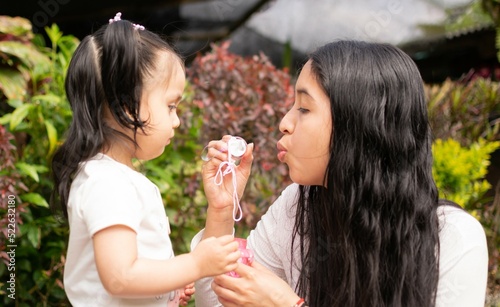 Mother teaches her little daughter how to do bubbles. Mother and daughter play together in the garden