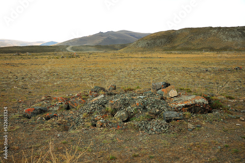 A small stone mound plundered by ancient marauders in an autumn valley at the foot of a mountain range. photo