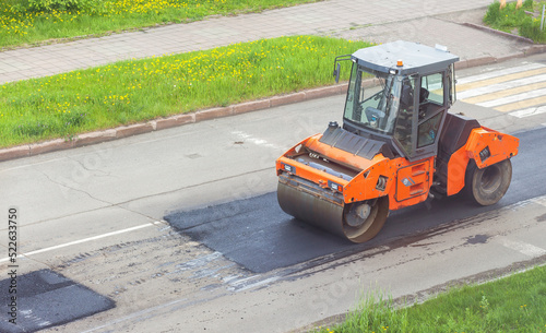 Road works on asphalt laying. Workers in vests are laying patches and rolling them out with a large roller.