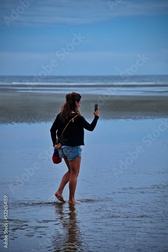 Mature woman walking on the beautiful beach and using mobile phone