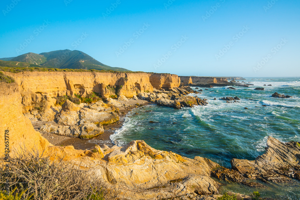 Rocky cliffs by the ocean., turquoise colored water, and clear blue sky