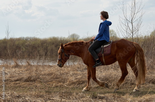 Woman in casual clothes rides a horse in early spring