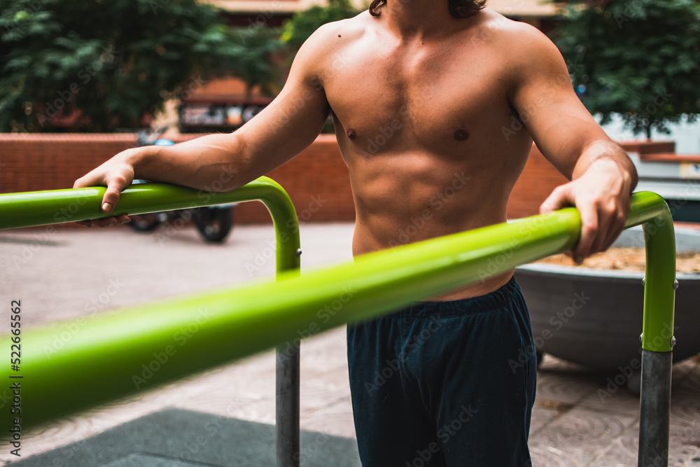 Fototapeta premium Close up of a non recognizable shirtless muscular caucasian man exercising calisthenics in outdoor bars.