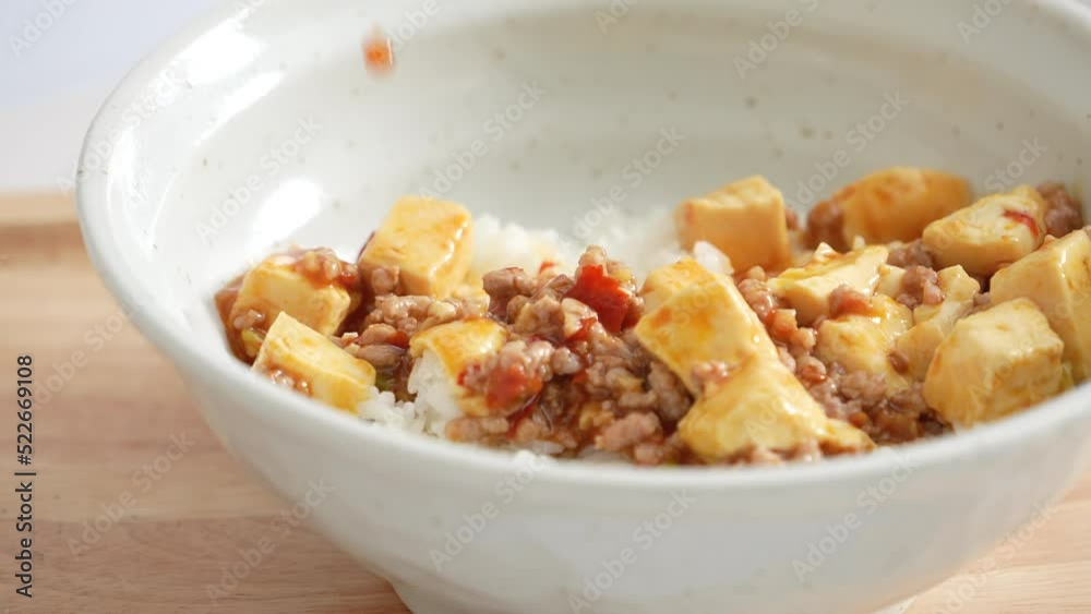 Pouring stir-fried mapo tofu with hot spicy sauce over white rice in a bowl at home Pouring stir-fried mapo tofu with hot spicy sauce over white rice in a bowl at home