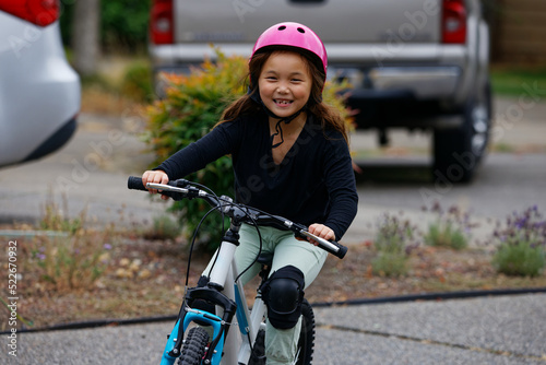 A young girl wearing a pink helmet and black knee pads riding a bicycle with a joyful expression on her face. photo