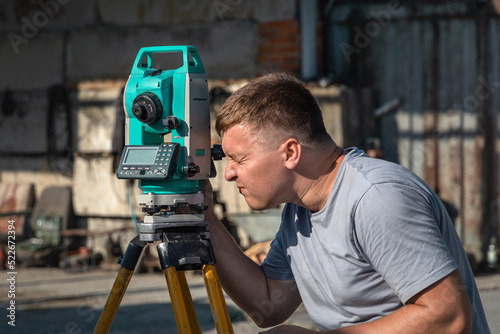 Portrait of a young man next to a total station in the open air. A male construction worker on an open construction site. A surveyor working with a total station.