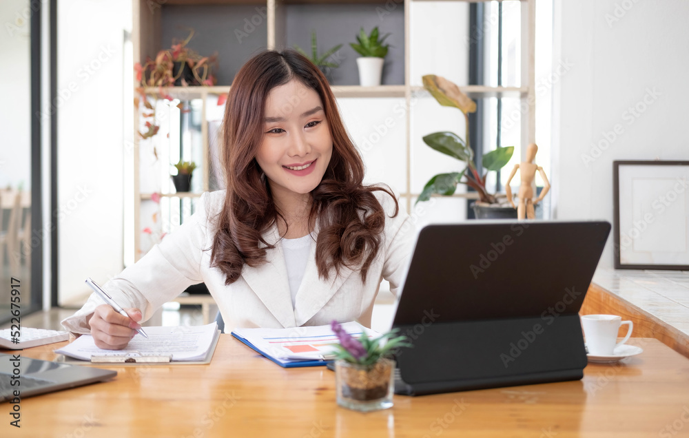 Beautiful Asian businesswoman analyzes charts using laptop calculator at the office.