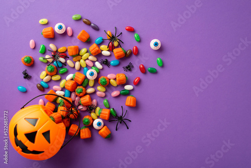 Halloween concept. Top view photo of pumpkin basket with candies eyes and spiders on isolated violet background