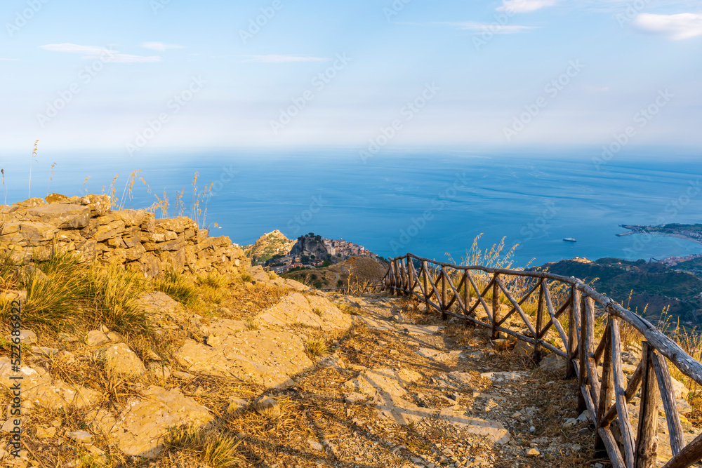 mountain landscape with a hiking trail leading to a mountain town and beautiful blue seashore far away