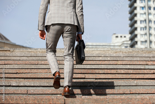 Man in a business suit with leather briefcase climbing stone stairs in city, male legs in motion on the steps. Concept of career, success, moving to the top, official or businessman