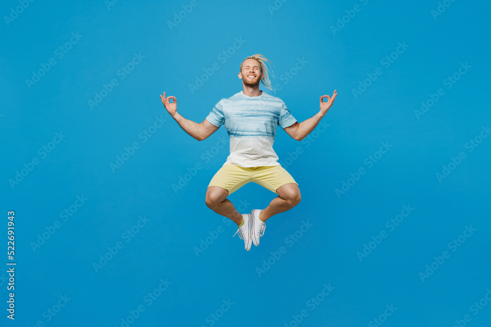Full body spiritual young blond man with dreadlocks 20s he wear white t-shirt hold spread hands in yoga om aum gesture relax meditate try to calm down isolated on plain pastel light blue background.